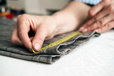Cropped hands of man measuring fabric on table