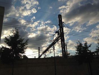 Low angle view of electricity pylon against cloudy sky