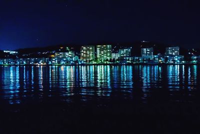 Illuminated buildings by sea against sky at night