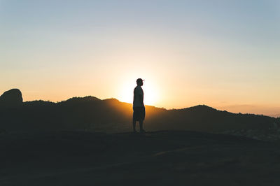 Man standing on hill against mountain during sunset