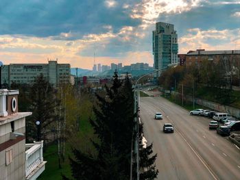 Cars on road by buildings in city against sky during sunset