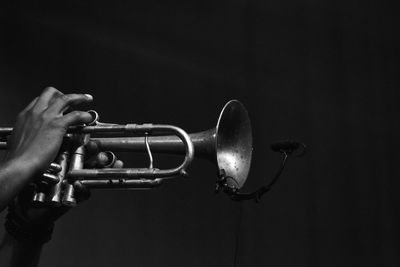 Cropped hand playing trumpet against black background