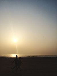 Silhouette people on beach against sky during sunset