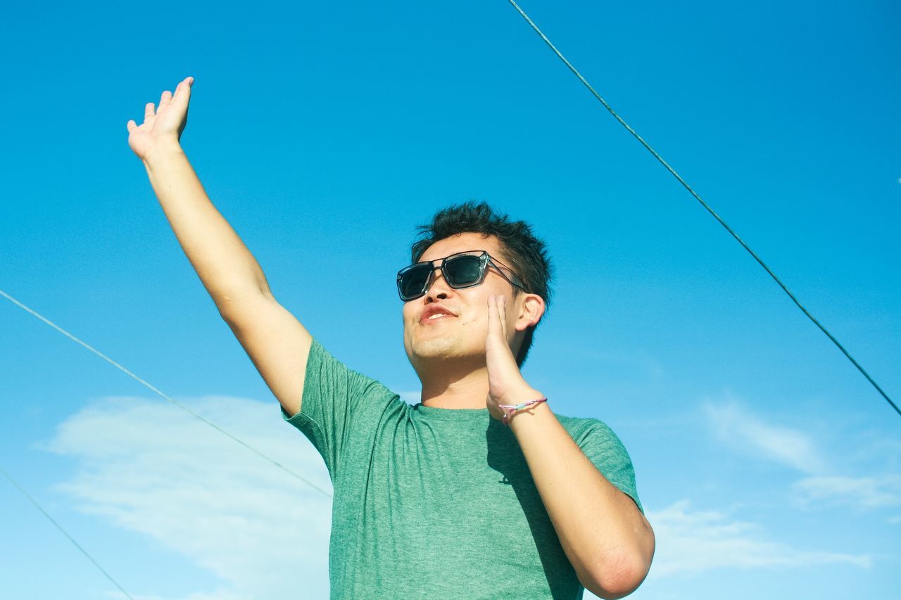 LOW ANGLE VIEW OF SMILING YOUNG WOMAN AGAINST SKY