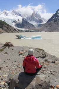 Rear view of woman sitting and meditating on rock against mountain