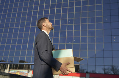 Businessman carrying box by office building on sunny day