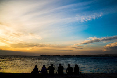 Silhouette people on beach against sky during sunset