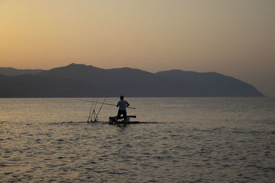 Silhouette man in sea against sky during sunset