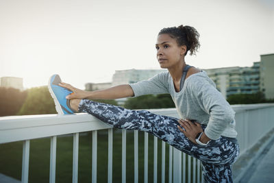 Woman stretching leg on railing at sidewalk