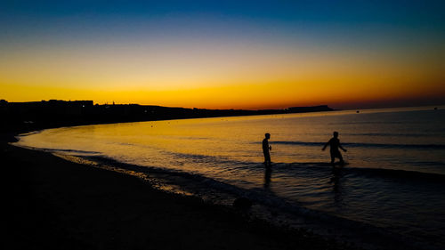 Silhouette people standing on beach against sky during sunset