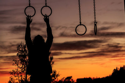 Silhouette person hanging on gymnastic rings against orange sky