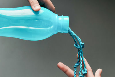 Cropped image of hands holding bottle and ropes over gray background