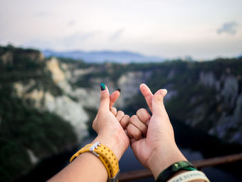 Close-up of hand holding hands against sky