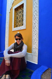 Portrait of young woman sitting against building at majorelle garden