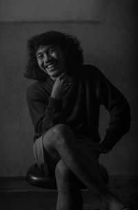 Portrait of smiling young woman sitting against wall