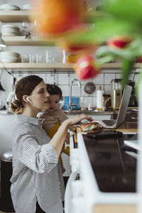 Female entrepreneur with male toddler working on laptop at home