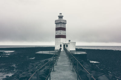 Lighthouse amidst sea and buildings against sky