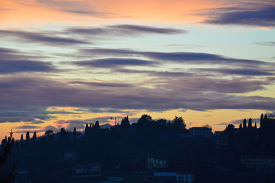 Silhouette city against dramatic sky during sunset