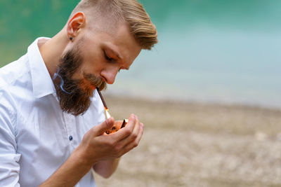 Portrait of a handsome bearded guy, lights a cigarette with a lighter outdoors