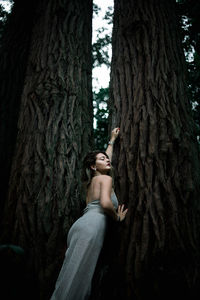 Sensual woman standing by tree trunk