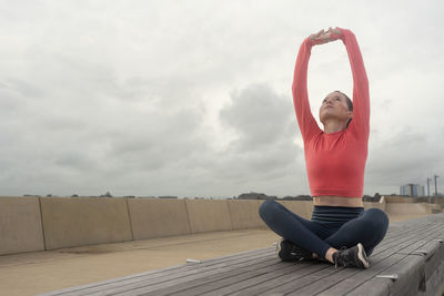 Sporty woman sitting doing an arm stretch, outdoor fitness.