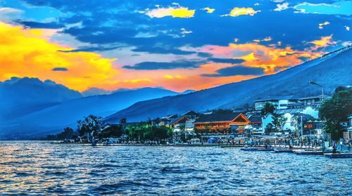 Houses by river and buildings against sky at sunset