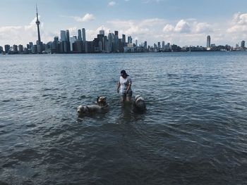 High angle view of young woman with dogs standing in river against sky