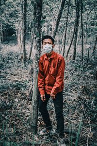 Portrait of man standing by tree trunk in forest