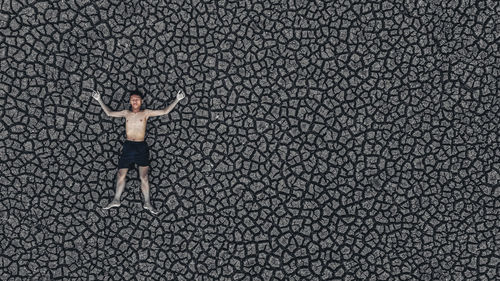 High angle view of shirtless boy with arms outstretched lying on cracked land