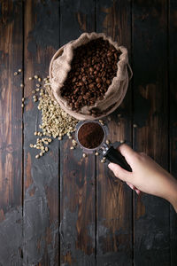 Cropped hand holding portafilter over coffee beans