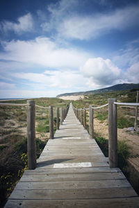 Pier on jetty leading towards lake against sky