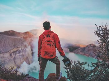 Rear view of man standing on rock against sky