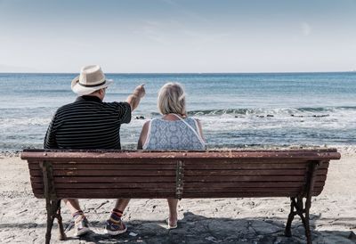 Rear view of couple sitting on beach against sky