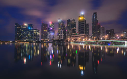 Illuminated buildings by river against sky at night