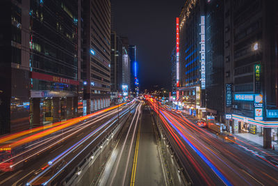 Light trails on city street amidst buildings at night