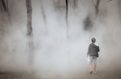 Rear view of boy waling amidst fog in forest