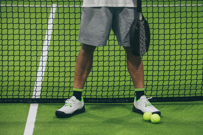 Closeup view of male legs with shorts in a padel tennis court standing near the net. young athlete