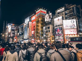 People walking on illuminated street amidst buildings in city at night