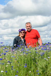 Married couple in the middle of a colorful field of cornflowers enjoying summer, sky full of clouds