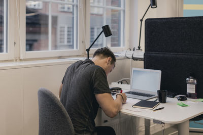 Businessman writing while using laptop at desk in creative office