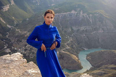 Brunette woman in a blue long dress stands on the edge of the sulak canyon in the evening at sunset