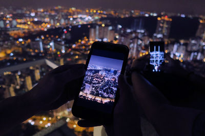 Cropped image of friends photographing illuminated cityscape through smart phone