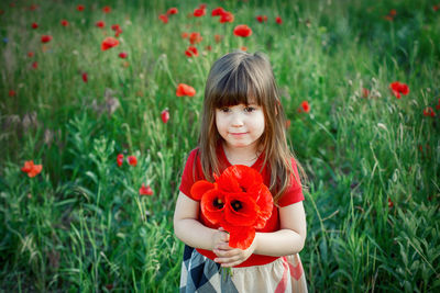 Portrait of smiling girl holding red flower in field