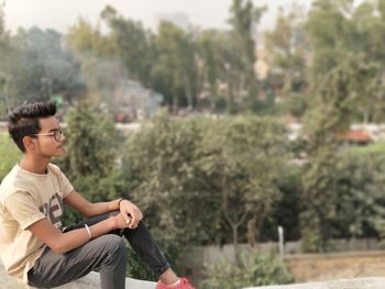 Teenage boy sitting against trees