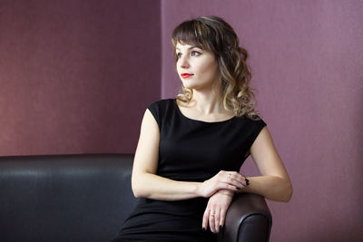 Portrait of a young woman sitting against wall