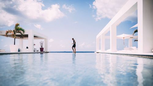 Side view of man walking at infinity pool against cloudy sky