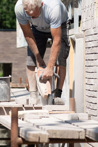 A grayhaired man saw bricks with a concrete saw of the right size for subsequent