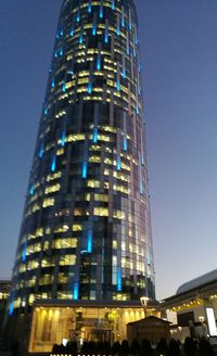 Low angle view of skyscrapers lit up against blue sky