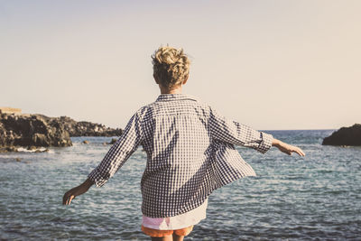 Rear view of cheerful boy standing at beach against clear sky