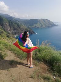 Portrait of woman with rainbow flag standing at beach